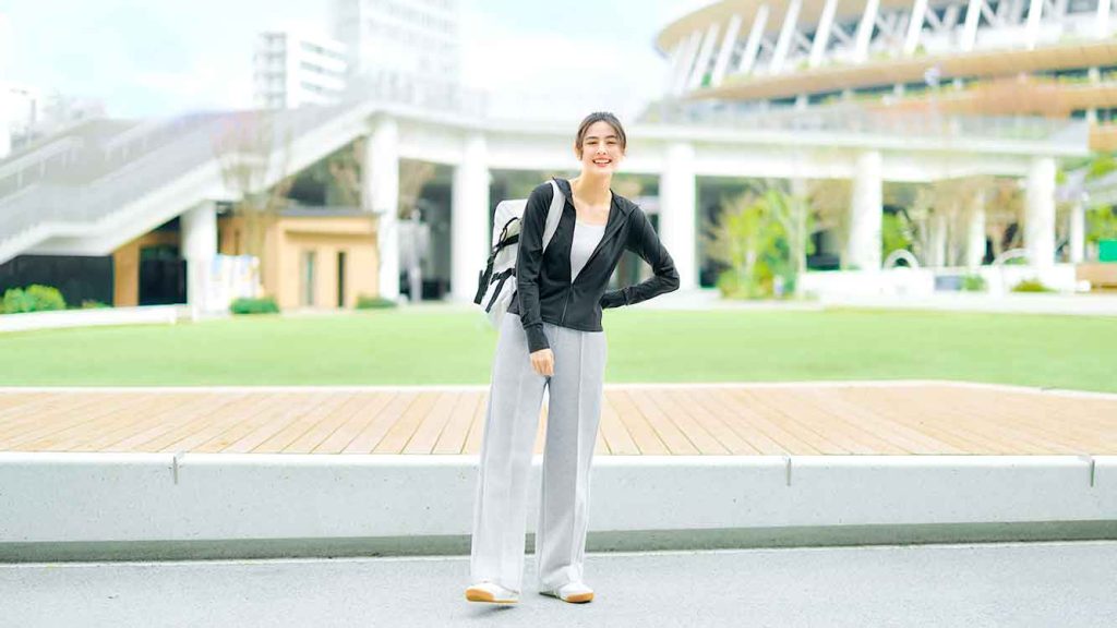 Model wanita mengenakan cardigan kerja navy proteksi sinar UV dari UNIQLO di depan gedung perkantoran modern